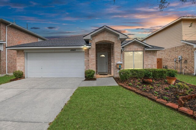 ranch-style home featuring brick siding, a yard, a shingled roof, a garage, and driveway