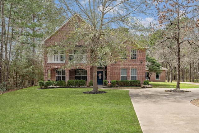 view of front facade with driveway, brick siding, a front yard, and a balcony