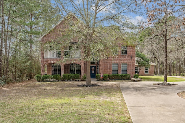 view of front of home featuring driveway, brick siding, a front yard, and a balcony