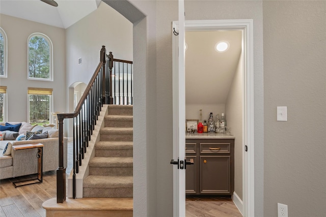 stairs with arched walkways, a dry bar, ceiling fan, wood finished floors, and high vaulted ceiling