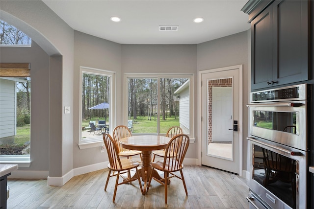 dining area with light wood-type flooring, visible vents, arched walkways, and recessed lighting