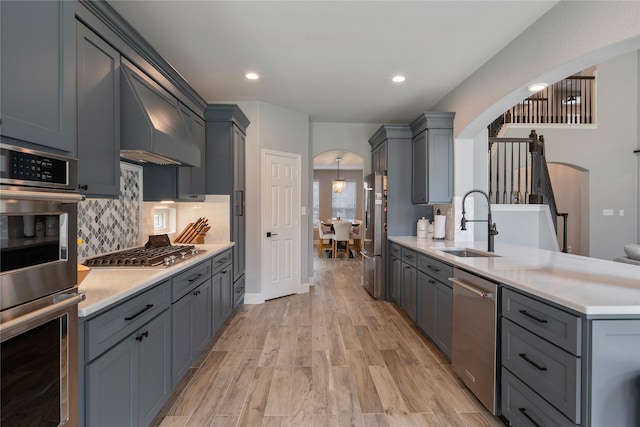 kitchen featuring arched walkways, stainless steel appliances, ventilation hood, and light countertops