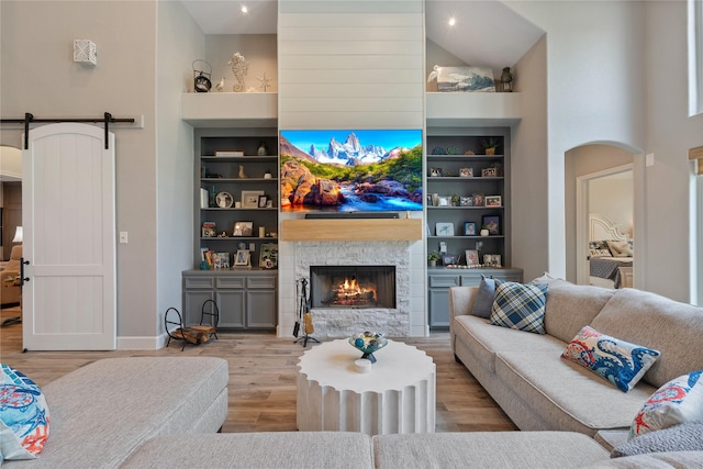 living room featuring a towering ceiling, a barn door, built in shelves, and wood finished floors