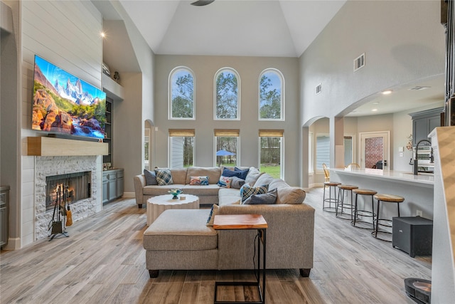 living area with arched walkways, light wood-type flooring, visible vents, and a stone fireplace