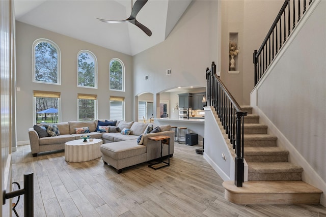 living room featuring arched walkways, visible vents, stairway, light wood-style flooring, and a ceiling fan