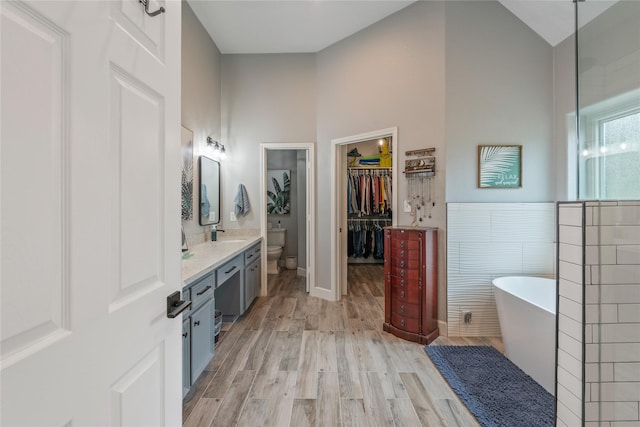 full bath featuring toilet, wood finished floors, vanity, tile walls, and a soaking tub