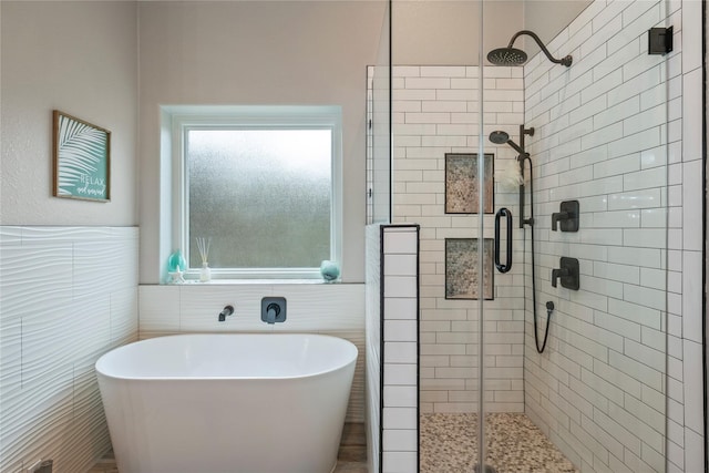 bathroom with a wainscoted wall, a stall shower, a freestanding tub, and tile walls