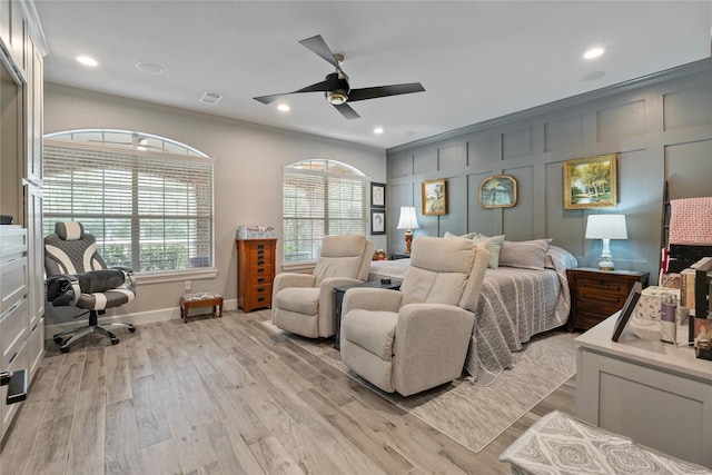 bedroom featuring ceiling fan, light wood-style flooring, a decorative wall, visible vents, and crown molding