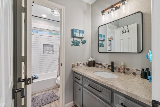 full bath with toilet, a textured wall, shower / bathtub combination with curtain, and vanity