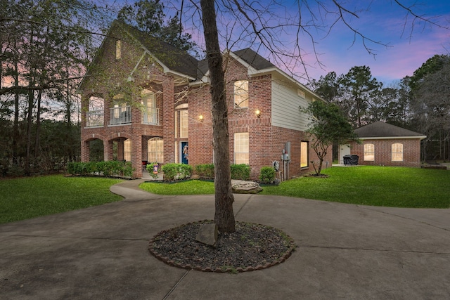 view of front facade featuring curved driveway, brick siding, a yard, and a balcony