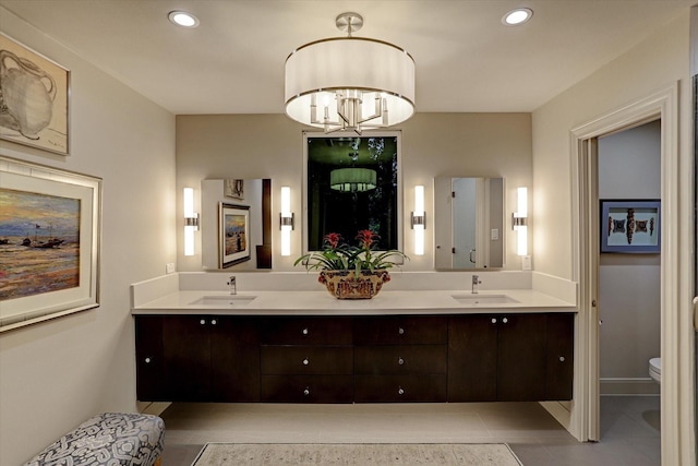 bathroom with toilet, double vanity, a chandelier, and a sink