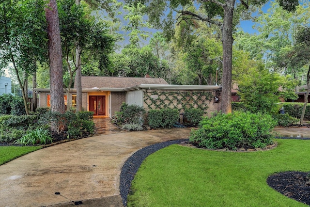 mid-century inspired home with a front yard, concrete driveway, brick siding, and a chimney