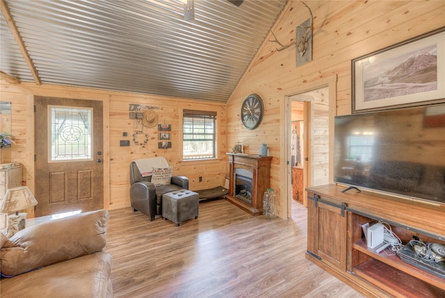 living area with light wood-type flooring, wood walls, a fireplace, and lofted ceiling