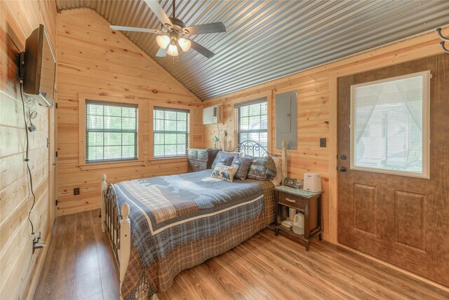 bedroom featuring lofted ceiling, a wall unit AC, wooden walls, wood finished floors, and electric panel