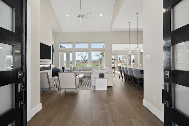 living area with dark wood finished floors, recessed lighting, baseboards, and a towering ceiling