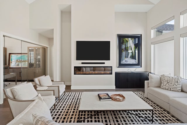 living room featuring a glass covered fireplace, a high ceiling, baseboards, and wood finished floors