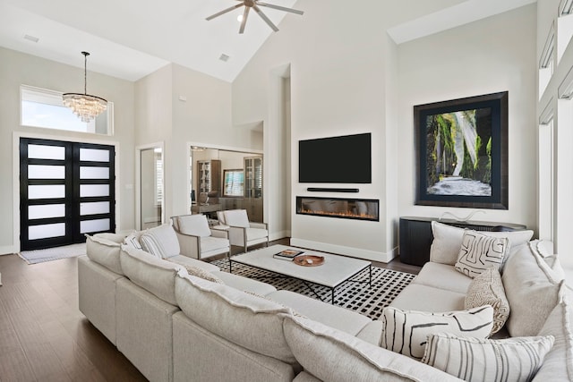 living room featuring a glass covered fireplace, ceiling fan with notable chandelier, high vaulted ceiling, and wood finished floors