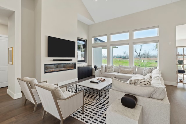 living room featuring a glass covered fireplace, wood finished floors, baseboards, and high vaulted ceiling