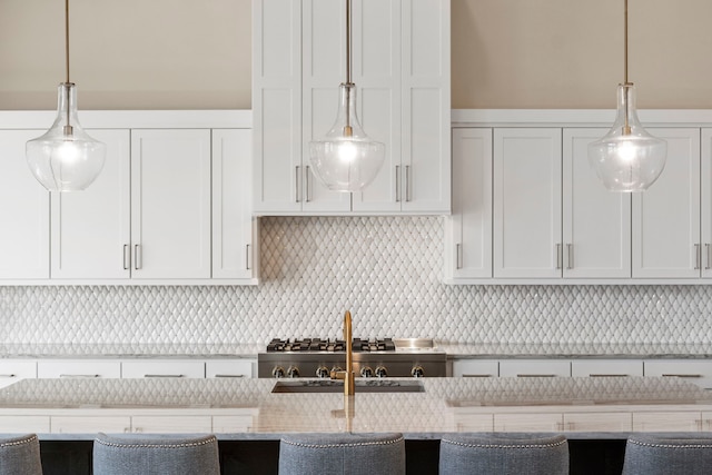 kitchen featuring light stone countertops, a sink, white cabinetry, decorative light fixtures, and backsplash