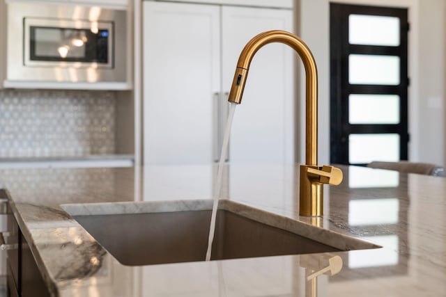 interior details with stainless steel microwave, white cabinets, backsplash, and a sink