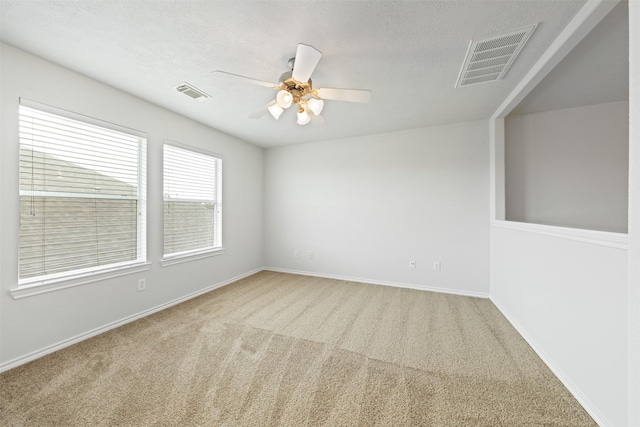 carpeted empty room featuring a ceiling fan, visible vents, a textured ceiling, and baseboards