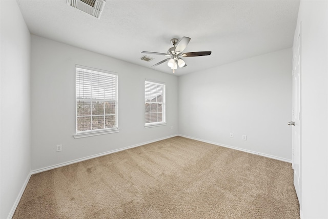 carpeted spare room with a ceiling fan, visible vents, and baseboards