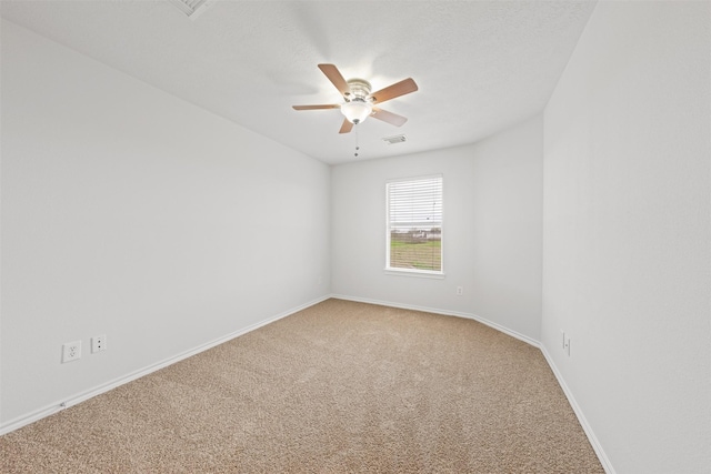 empty room with a textured ceiling, light colored carpet, a ceiling fan, baseboards, and visible vents