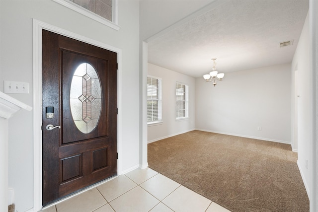 entryway featuring a chandelier, light tile patterned flooring, light carpet, visible vents, and baseboards