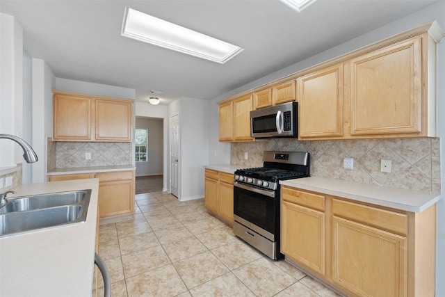 kitchen featuring light tile patterned flooring, light brown cabinets, a sink, appliances with stainless steel finishes, and tasteful backsplash