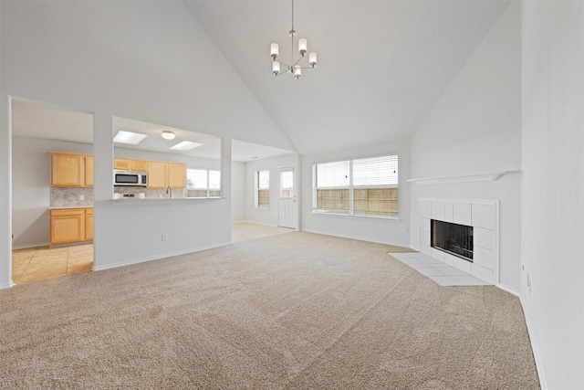 unfurnished living room with baseboards, a tile fireplace, light colored carpet, an inviting chandelier, and high vaulted ceiling