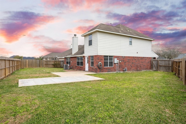 rear view of house featuring cooling unit, brick siding, a lawn, a chimney, and a patio area