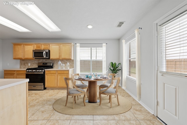 kitchen with stainless steel appliances, visible vents, light countertops, light brown cabinetry, and tasteful backsplash