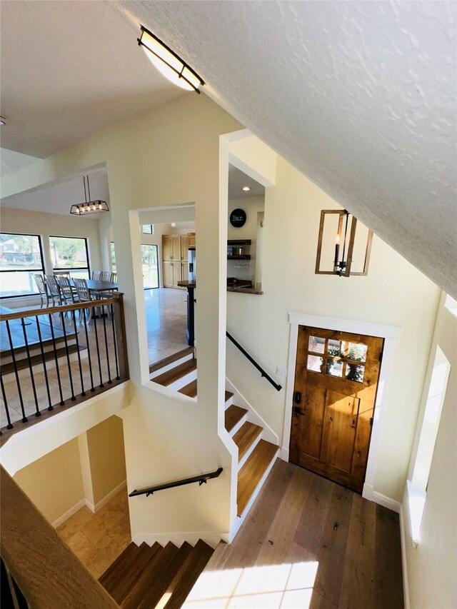 foyer entrance with baseboards, wood finished floors, stairs, vaulted ceiling, and a textured ceiling