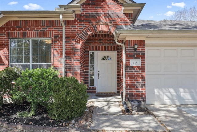 property entrance with a garage, brick siding, and roof with shingles