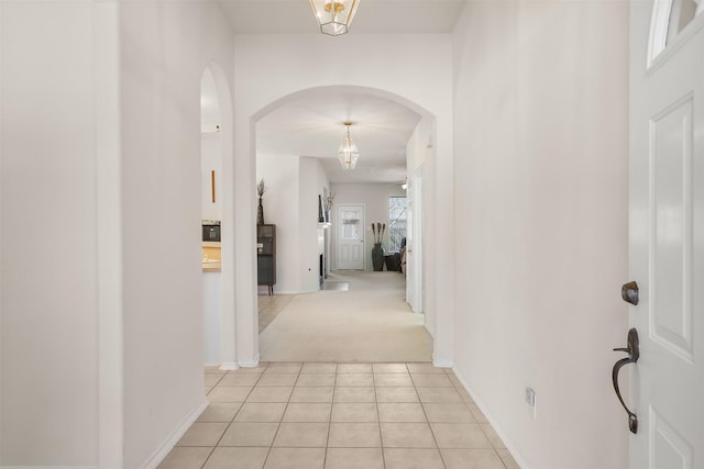 hallway featuring arched walkways, light tile patterned flooring, light carpet, and baseboards