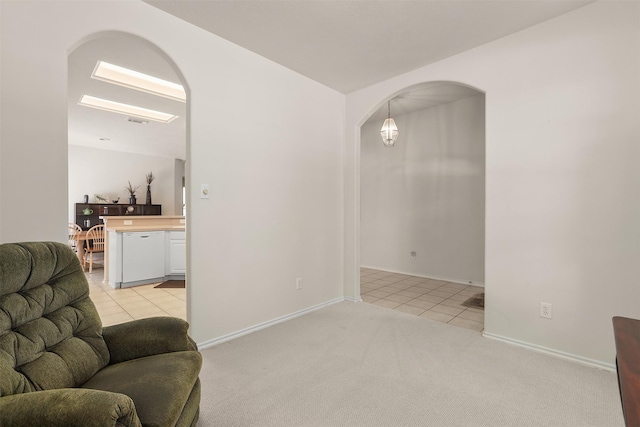 living area featuring light carpet, light tile patterned floors, baseboards, and arched walkways