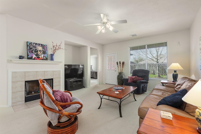 carpeted living room featuring ceiling fan, a tiled fireplace, and visible vents