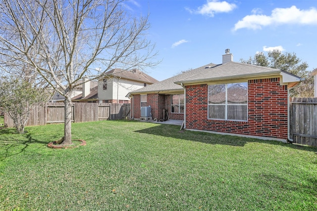 back of house with a fenced backyard, a chimney, cooling unit, a yard, and brick siding