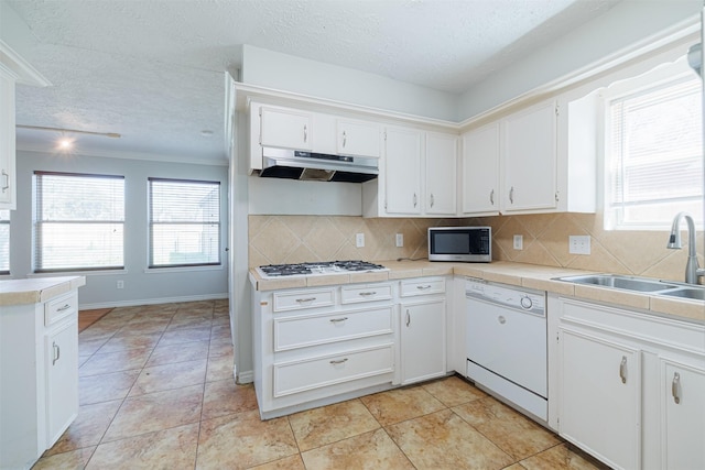 kitchen featuring white appliances, a sink, under cabinet range hood, white cabinetry, and tasteful backsplash