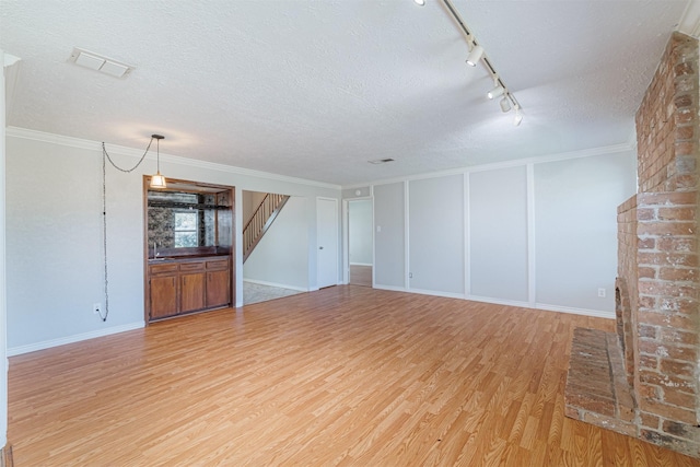 unfurnished living room with visible vents, ornamental molding, a textured ceiling, stairway, and light wood finished floors