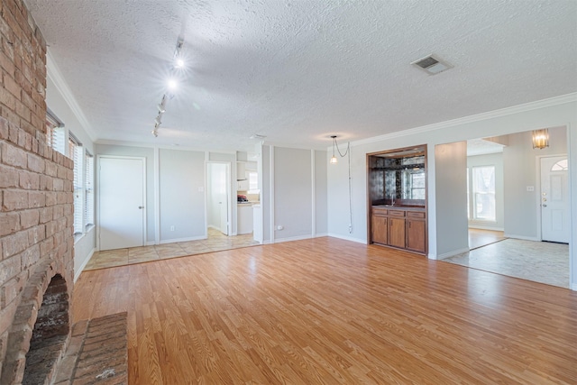 unfurnished living room featuring visible vents, track lighting, crown molding, light wood-type flooring, and a textured ceiling