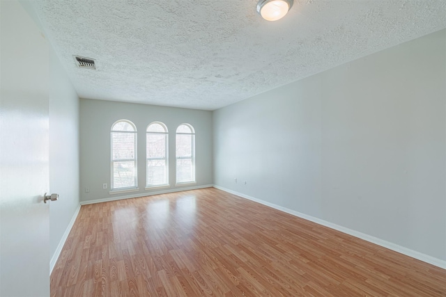 spare room featuring visible vents, light wood-style flooring, a textured ceiling, and baseboards