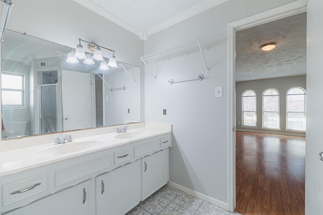 bathroom with a textured ceiling, crown molding, a shower stall, and a sink