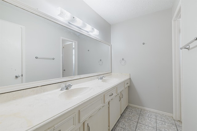 full bathroom with a sink, baseboards, a textured ceiling, and double vanity