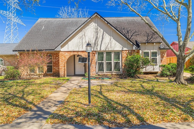 english style home featuring brick siding, a front yard, and a shingled roof