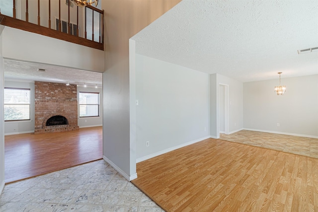 unfurnished living room featuring visible vents, a textured ceiling, wood finished floors, a fireplace, and a chandelier