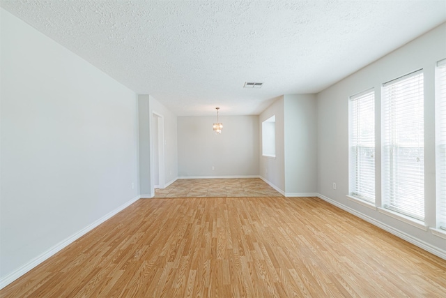 spare room with a notable chandelier, visible vents, light wood finished floors, and a textured ceiling