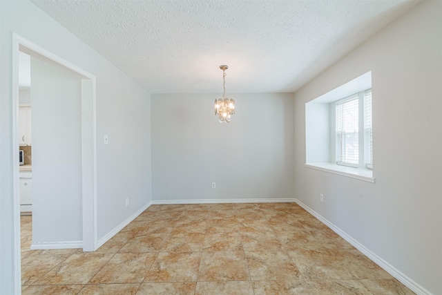 spare room with baseboards, a textured ceiling, and an inviting chandelier