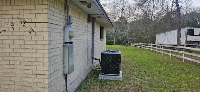 view of side of home with a lawn, fence, central AC, and brick siding