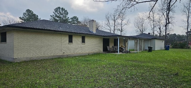 back of house with a yard, brick siding, and a chimney